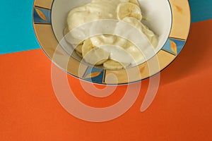 Bowl of sliced banana and yoghurt in a bowl on bright orange and