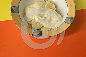Bowl of sliced banana and yoghurt in a bowl on bright orange and