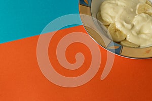 Bowl of sliced banana and yoghurt in a bowl on bright orange and