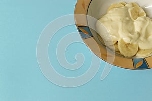 Bowl of sliced banana and yoghurt in a bowl on pastel blue background - minimal, copy space