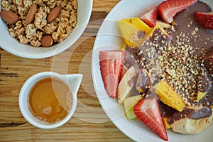 Bowl of sliced fruits and berries with chocolate souse and crushed walnuts with granola and orange juice photo