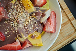 Bowl of sliced fruits and berries with chocolate souse and crushed walnuts standing on a wood board photo
