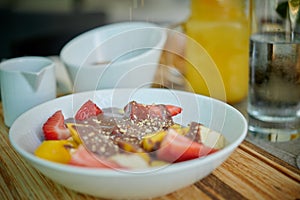 Bowl of sliced fruits and berries with chocolate souse and crushed walnuts standing on a wood board, orange juice