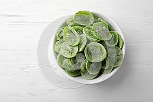 Bowl with slices of kiwi on wooden background, top view.