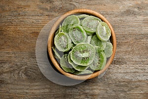 Bowl with slices of kiwi on wooden background, top view.