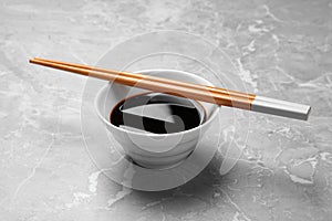 Bowl of soy sauce with chopsticks on background