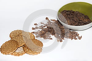 Bowl with spilled chocolate cereal and whole grain cookies on white background