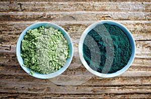 Bowl of spirulina algae powder and wheat sprout powder on wooden