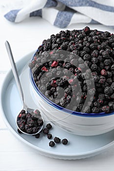 Bowl and spoon with dried blueberries on white wooden table, closeup