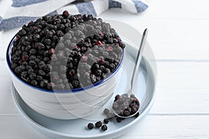 Bowl and spoon with dried blueberries on white wooden table, closeup. Space for text