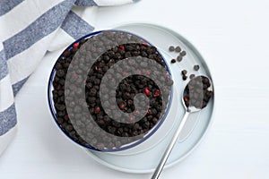 Bowl and spoon with dried blueberries on white wooden table, top view