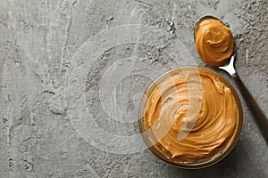 Bowl and spoon with peanut butter on gray background