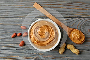 Bowl and spoon with peanut butter on wooden background