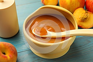 Bowl and spoon with tasty pureed baby food on light blue wooden table, closeup