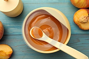 Bowl and spoon with tasty pureed baby food on light blue wooden table, flat lay