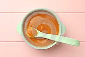 Bowl and spoon with tasty pureed baby food on pink wooden table, top view