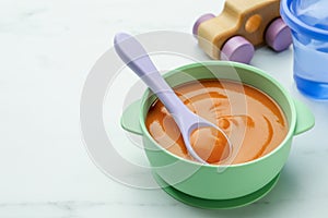 Bowl and spoon with tasty pureed baby food on white table, space for text