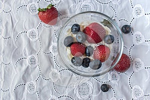 Bowl of strawberries and blueberries in whip cream on white linen tablecloth