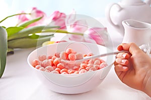 bowl with strawberry sweet corn balls. Delicious and healthy breakfast cereal. Kid hand take a spoon and eating