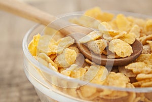 bowl of sugar-coated corn flakes and spoon for breakfast or snack over rustic wooden background.