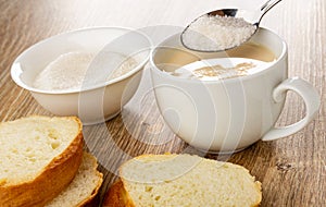 Bowl with sugar, slices of bread, spoon with sugar above white cup with fermented baked milk on wooden table