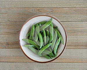 A bowl of sugar snap peas on a wood background photo