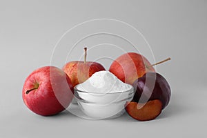Bowl with sweet fructose powder, ripe apples and plums on white background