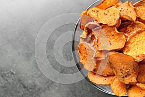 Bowl with sweet potato chips on grey table, top view.