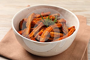 Bowl with sweet potato fries and rosemary on wooden table, closeup