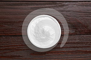 Bowl of sweet powdered fructose on black wooden table, top view