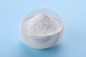 Bowl of sweet powdered fructose on light blue background