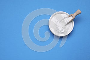 Bowl of sweet powdered fructose on light blue background, top view. Space for text