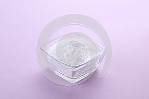 Bowl of sweet powdered fructose on light purple background