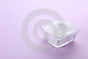 Bowl of sweet powdered fructose on light purple background. Space for text