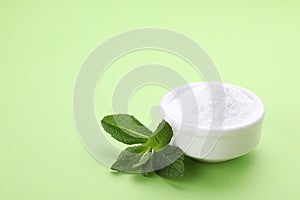 Bowl of sweet powdered fructose and mint leaves on light green background. Space for text
