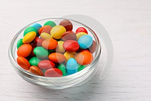 Bowl with tasty colorful candies on white wooden table, closeup