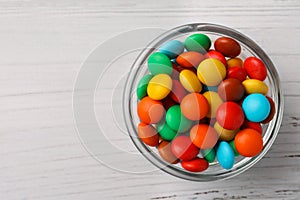 Bowl with tasty colorful candies on white wooden table, top view. Space for text