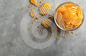 Bowl with tasty crispy potato chips on grey table