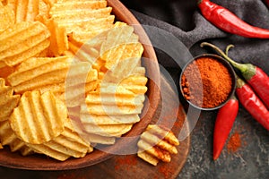 Bowl with tasty crispy potato chips on wooden board, closeup