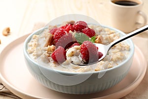 Bowl with tasty oatmeal porridge with nuts and raspberries on table. Healthy meal