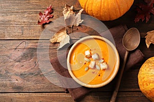 Bowl with tasty pumpkin cream soup on wooden table, flat lay. Space for text