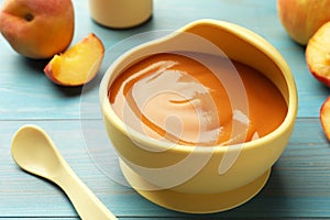 Bowl of tasty pureed baby food and ingredients on light blue wooden table, closeup