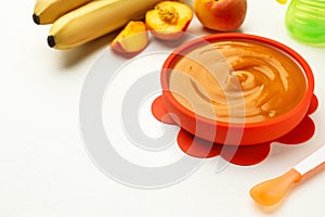 Bowl of tasty pureed baby food and ingredients on white table. Space for text