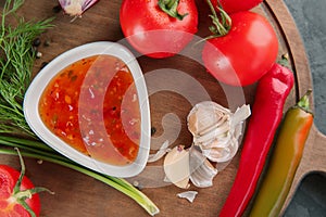 Bowl with tasty sauce and vegetables on wooden board