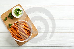 Bowl with tasty sweet potato fries and sauce on wooden background, top view