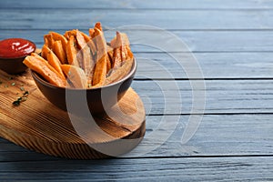 Bowl with tasty sweet potato fries on wooden background