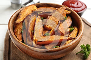 Bowl with tasty sweet potato fries on wooden board