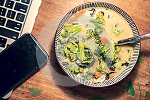 Bowl of Thai curry soup next to laptop and phone photo