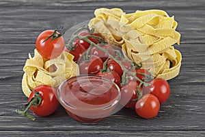 Bowl of tomato sauce, cherry tomatoes and italian pasta on wooden background