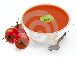 Bowl with tomato soup gazpacho, tomatoes, basil leaf and spoon. Isolated on white background. Mediterranean diet food composed of